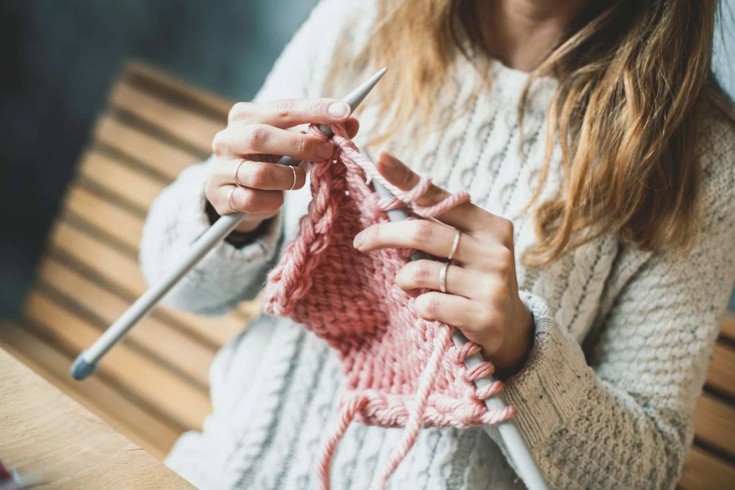 Person knitting pink yarn with needles in a softly lit room