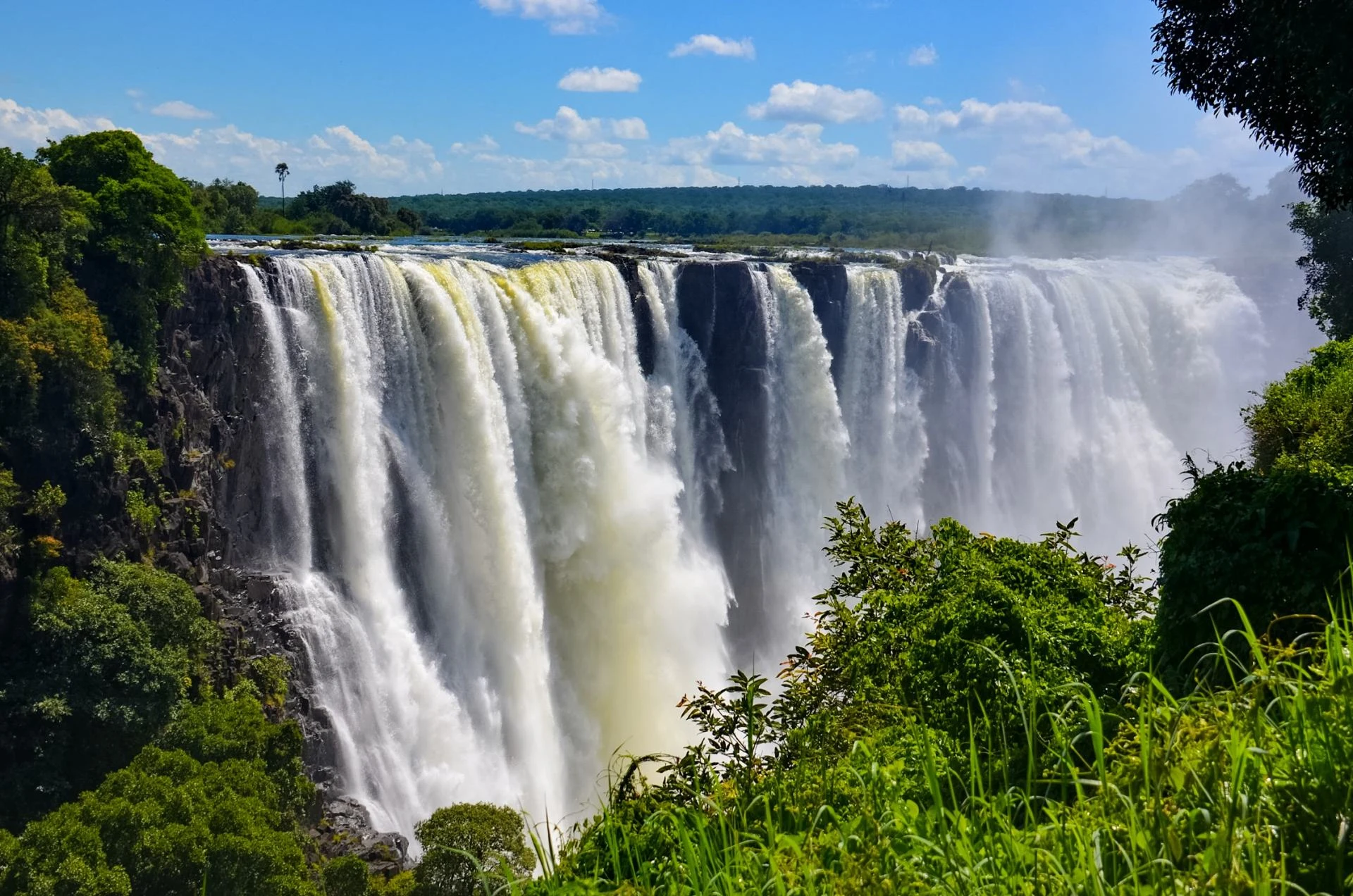Wide waterfall flowing through a green gorge