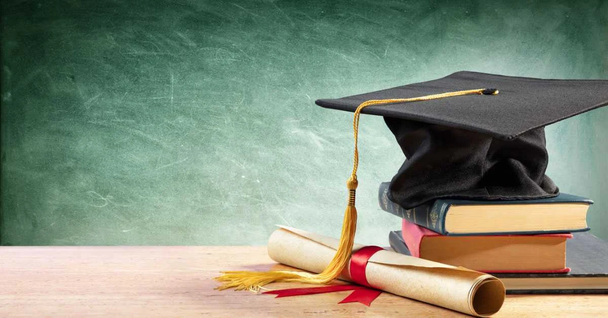 Graduation cap, diploma and books arranged in front of a classroom chalkboard