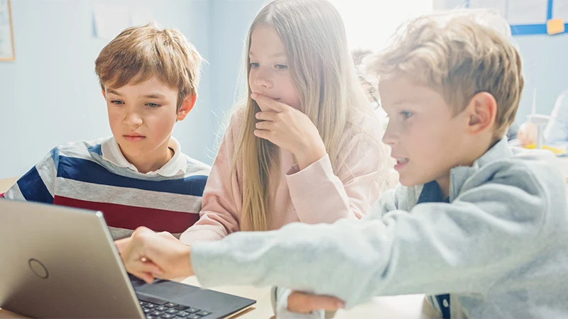 Teacher helping students use a laptop