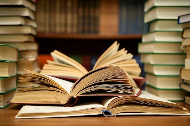 Open book surrounded by stacks of books